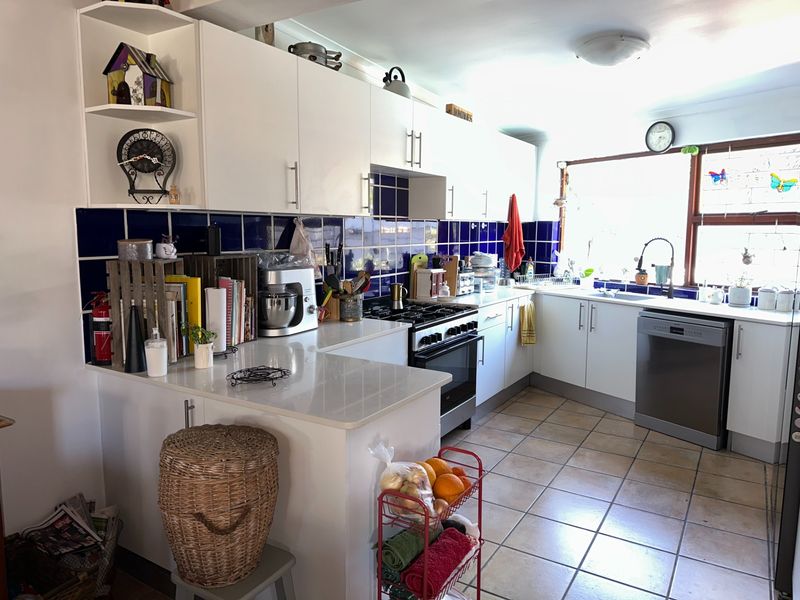 Functional kitchen featuring white cabinetry, stone countertops, blue tiled backsplash, gas stove, and integrated dishwasher with ceramic tiled flooring.