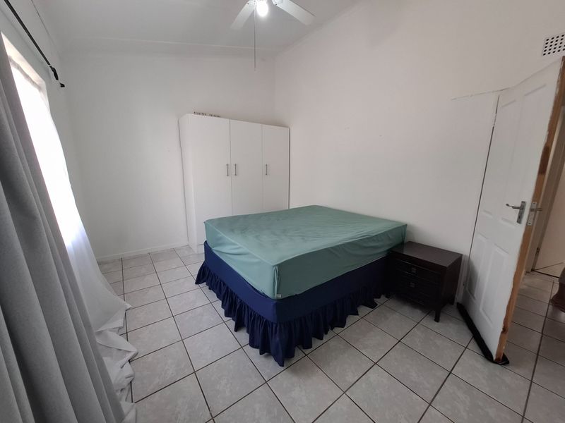 A bedroom featuring tiled flooring, a built-in wardrobe, and a ceiling fan, requiring minor cosmetic updates to the walls and door frame.