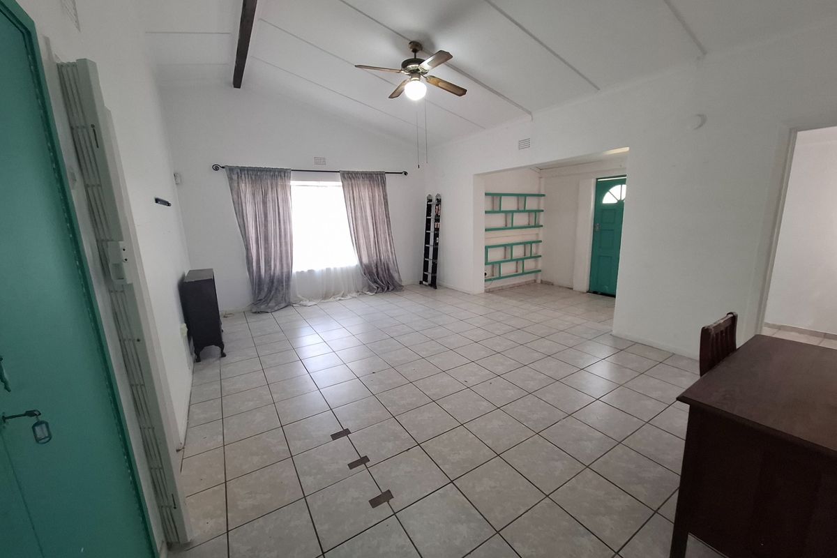Spacious living area featuring tiled flooring, a vaulted ceiling with an exposed beam, ceiling fan, and built-in shelving.