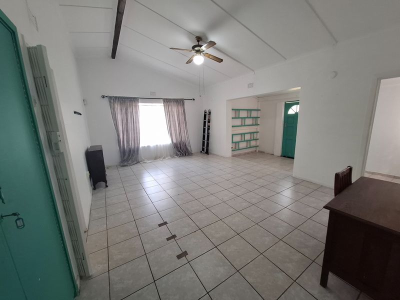 Spacious living area featuring tiled flooring, a vaulted ceiling with an exposed beam, ceiling fan, and built-in shelving.