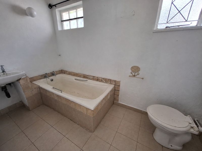 A dated bathroom featuring a built-in bathtub, wall-mounted basin, and toilet, requiring cosmetic updates and refurbishment to restore its functionality and appeal.