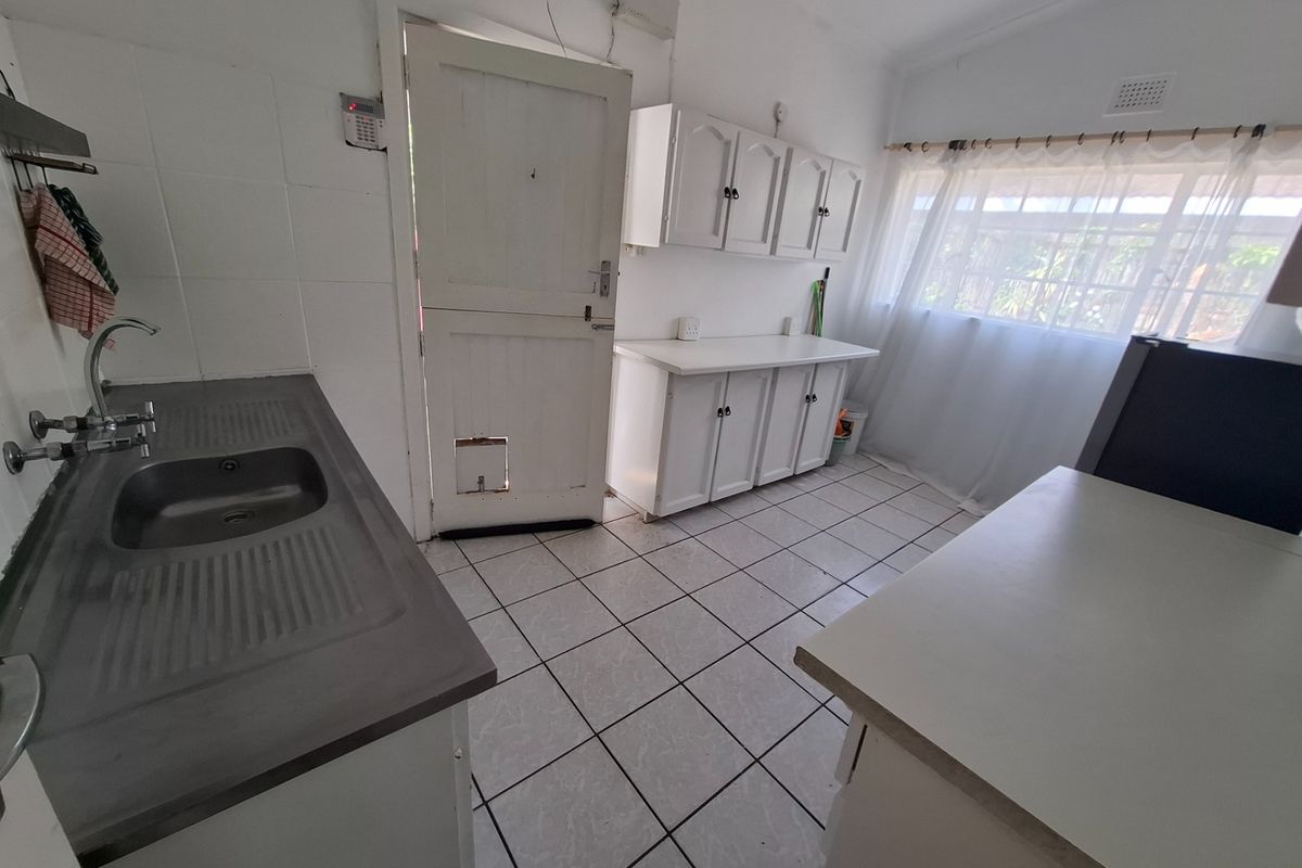 A functional kitchen featuring tiled flooring, built-in cabinetry, a stainless steel sink, and a stable door leading to the exterior.