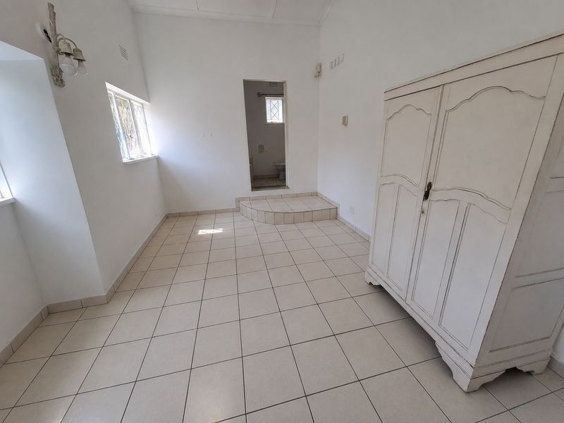A bright bedroom featuring tiled flooring, a raised platform area, and direct access to an en-suite bathroom.