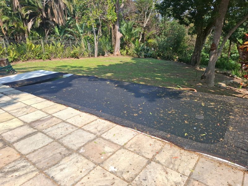 Outdoor pool area featuring stone paving and a safety cover, set against a backdrop of established trees and a garden.
