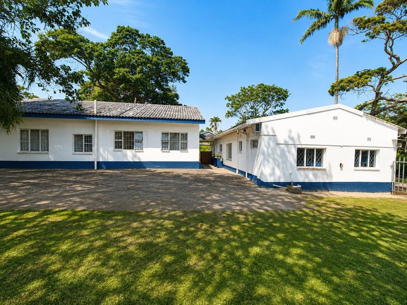 Rear view of the property featuring a large concrete driveway, established lawn, and white painted exterior walls with blue trim.