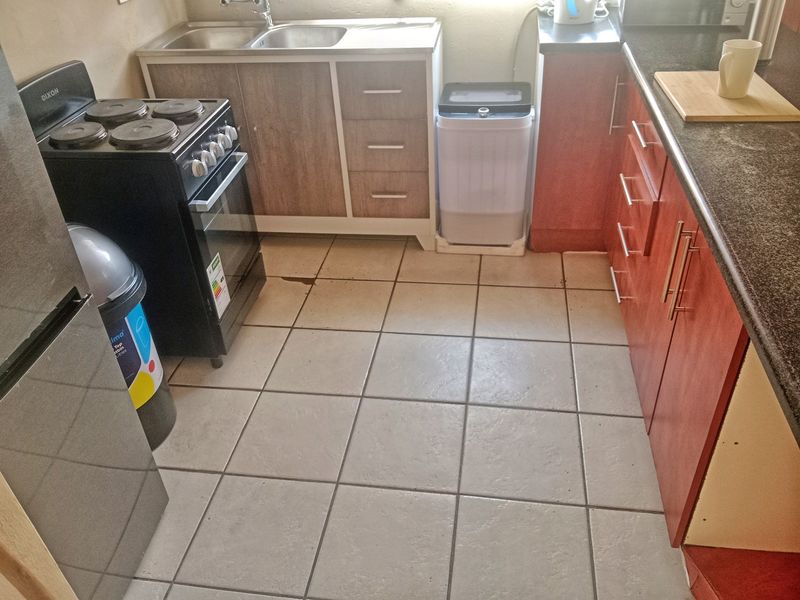 Compact kitchen featuring built-in cabinetry, laminate countertops, a stainless steel sink, and an electric stove with ceramic tiled flooring.