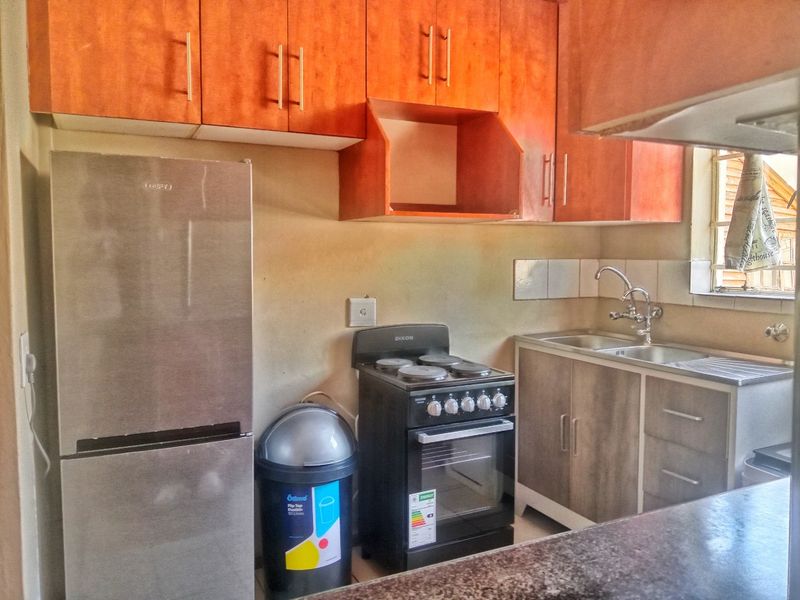 Compact kitchen featuring wooden cabinetry, stainless steel sink, tiled backsplash, and a freestanding stove, offering a functional layout for daily meal preparation.