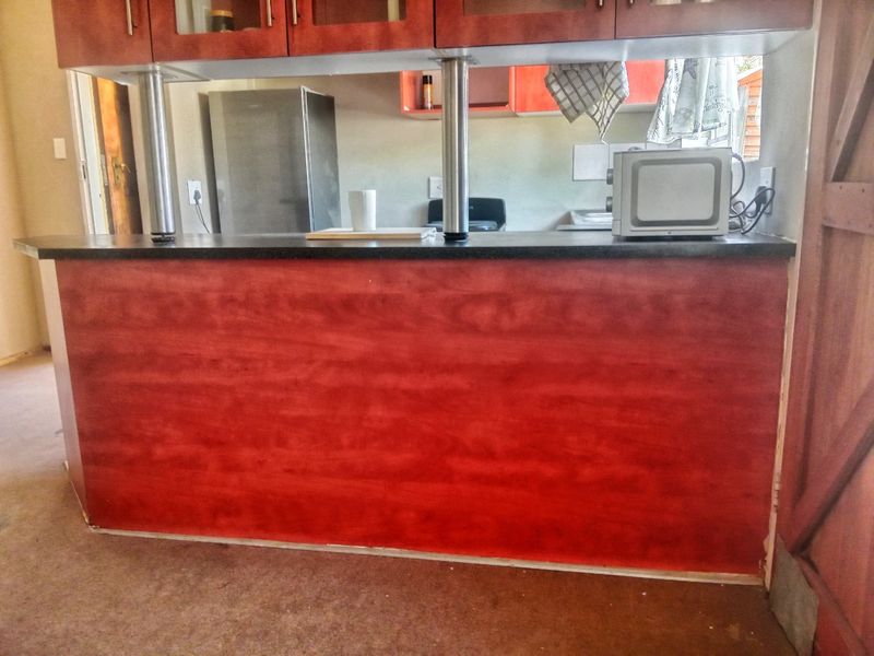 A kitchen featuring a breakfast bar with a dark countertop, stainless steel support columns, and reddish-toned built-in cabinetry.