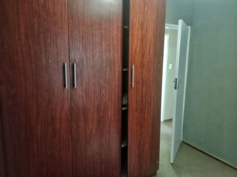A bedroom interior featuring a built-in wooden wardrobe and an open doorway leading to an adjacent space.