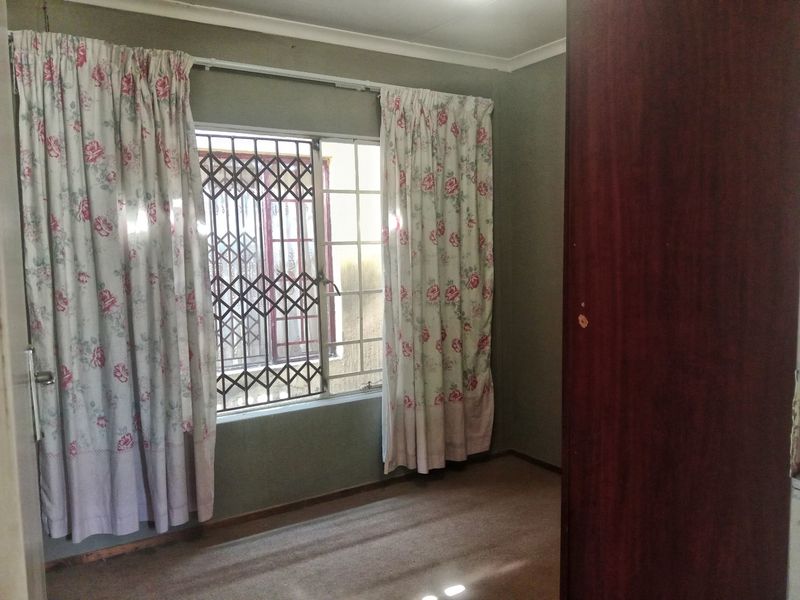 A vacant bedroom featuring a built-in cupboard, security gate on the window, and carpeted flooring.