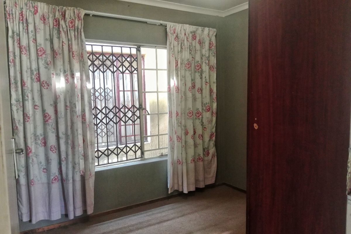 A vacant bedroom featuring a built-in cupboard, security gate on the window, and carpeted flooring.