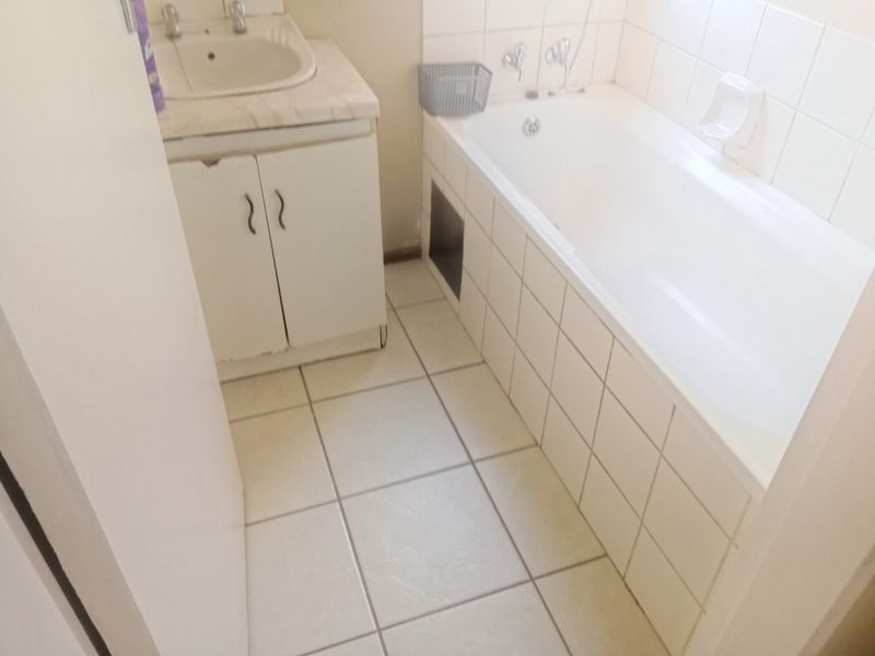 A dated bathroom featuring a built-in vanity with basin and a standard bathtub with tiled surround and flooring.