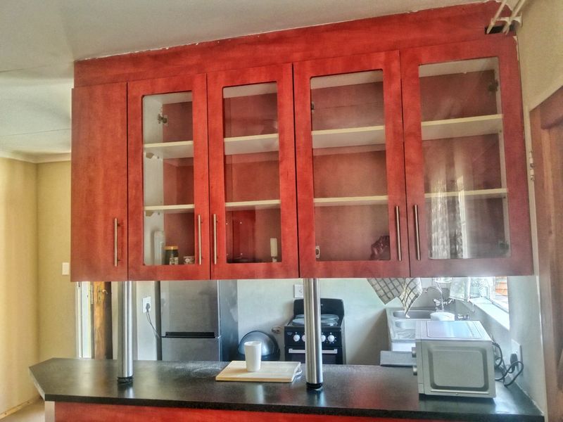 Kitchen area featuring red-toned cabinetry with glass inserts, a breakfast bar with stainless steel supports, and a functional sink and stove setup.