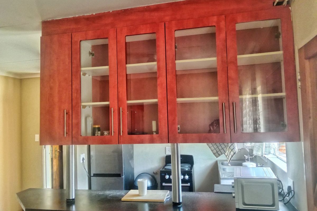 Kitchen area featuring red-toned cabinetry with glass inserts, a breakfast bar with stainless steel supports, and a functional sink and stove setup.
