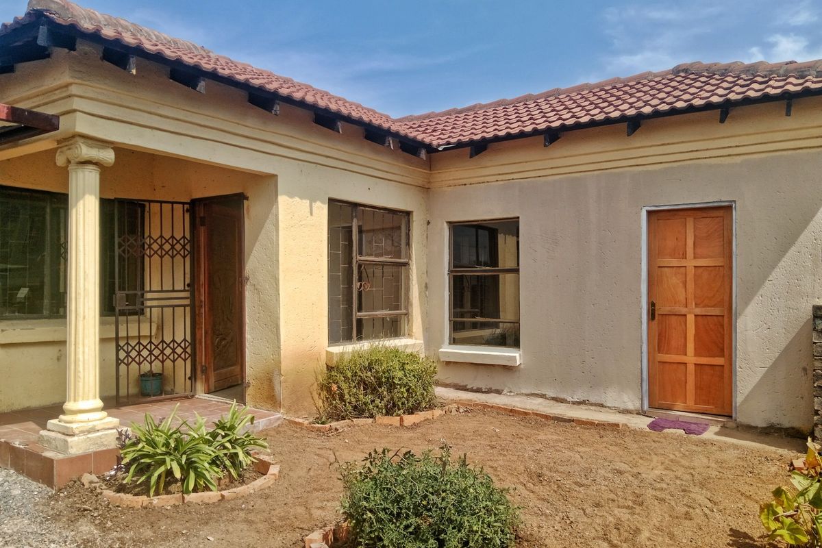Rear exterior view of the house featuring a tiled roof, concrete column, and basic garden area with visible maintenance requirements on the exterior walls.