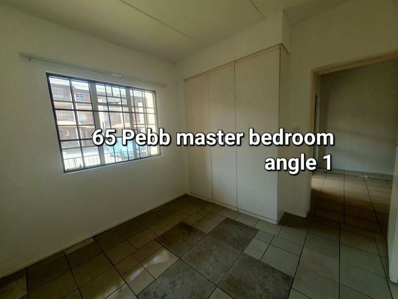 An empty bedroom featuring built-in cupboards, tiled flooring, and a window with security bars, offering a blank canvas for potential updates.