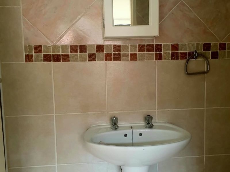 A bathroom featuring a pedestal basin, wall-mounted medicine cabinet, and decorative mosaic tile border on the wall.