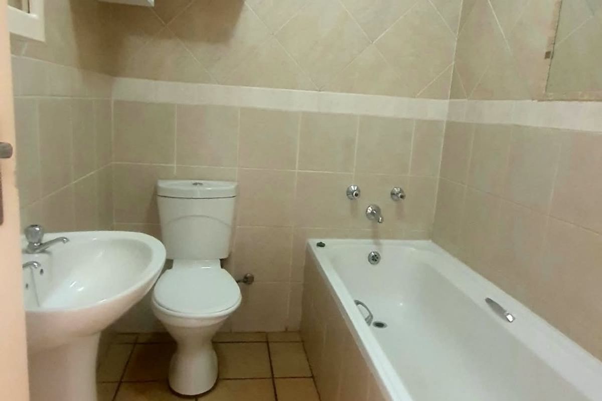 A functional bathroom featuring a pedestal basin, toilet, and bathtub with neutral wall and floor tiling.