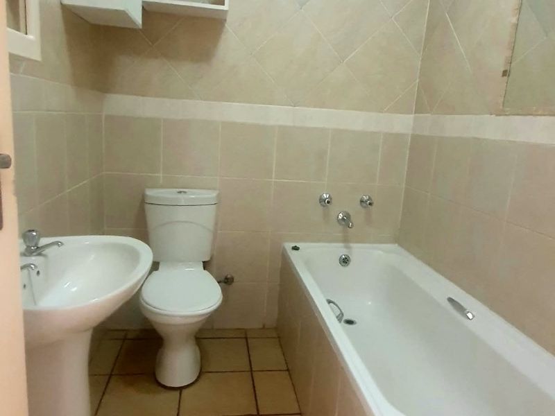 A functional bathroom featuring a pedestal basin, toilet, and bathtub with neutral wall and floor tiling.