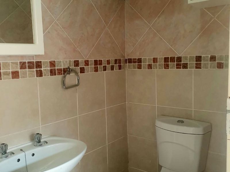 A compact en-suite bathroom featuring a pedestal washbasin, toilet, and neutral wall tiling with a decorative border.