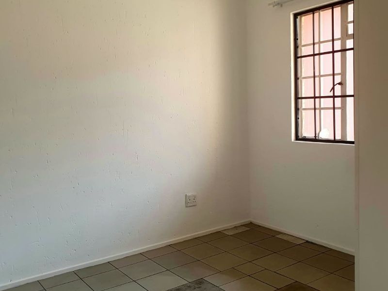 An empty bedroom featuring tiled flooring, a window with security bars, and a neutral wall finish.