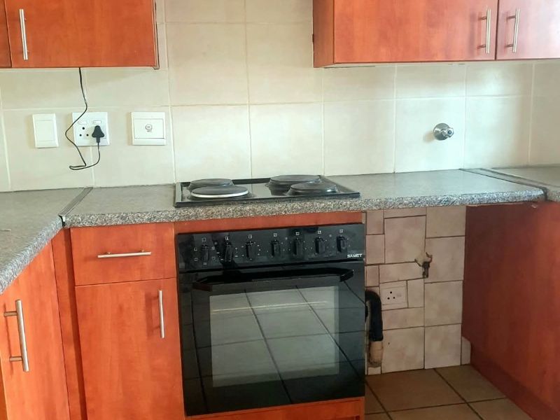 A dated kitchen featuring wood-tone cabinetry, laminate countertops, and a built-in oven with electric hob. The space requires minor repairs to tiling and finishes.