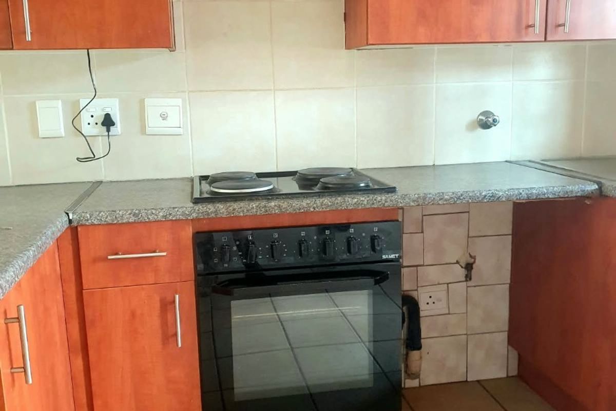 A dated kitchen featuring wood-tone cabinetry, laminate countertops, and a built-in oven with electric hob. The space requires minor repairs to tiling and finishes.