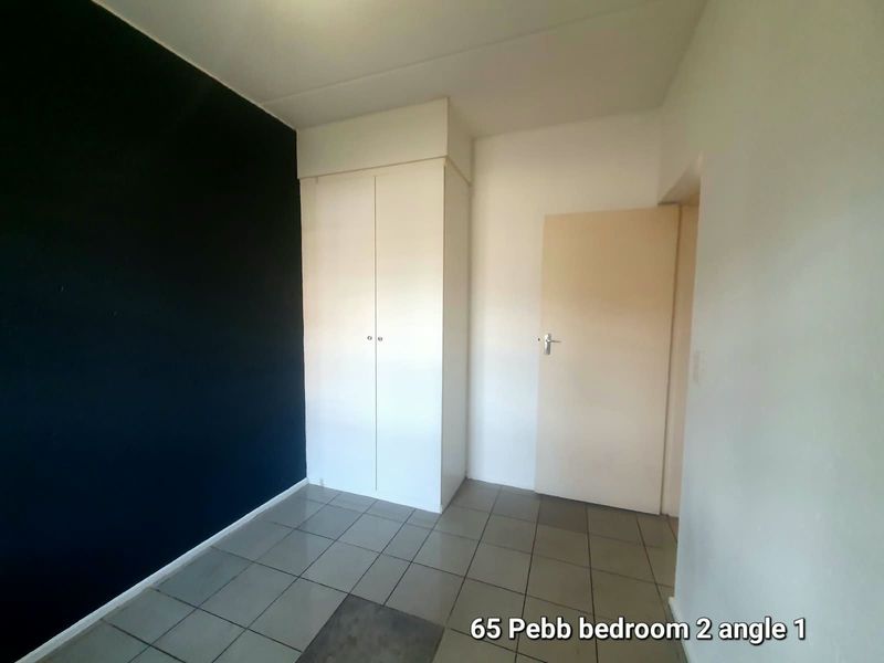 An empty bedroom featuring tiled flooring and a built-in wardrobe with a contrasting dark accent wall.