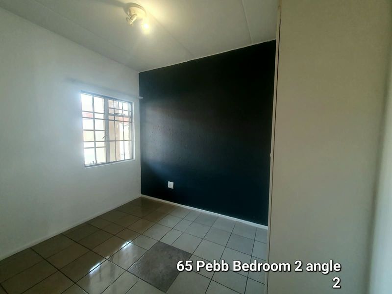 A vacant bedroom featuring tiled flooring, a dark accent wall, and a window fitted with security burglar bars.