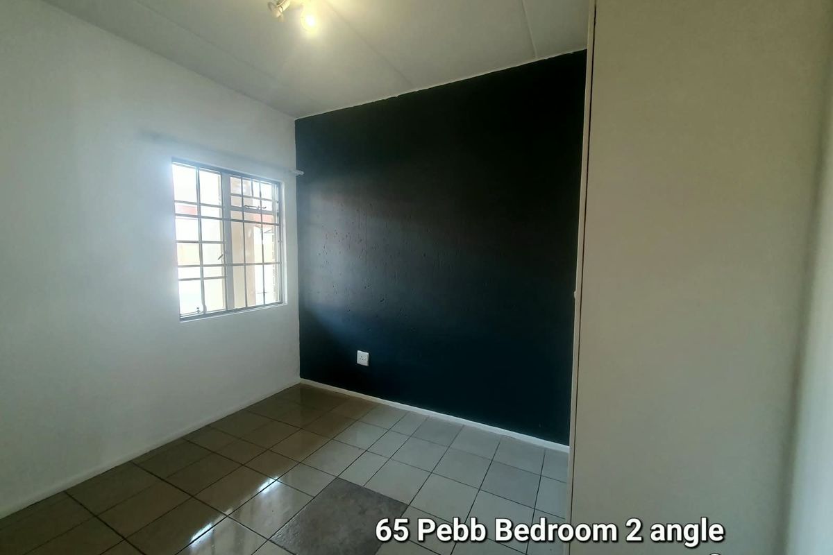 A vacant bedroom featuring tiled flooring, a dark accent wall, and a window fitted with security burglar bars.