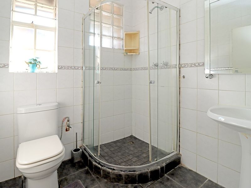 A functional bathroom featuring a corner shower enclosure, pedestal basin, and toilet with white wall tiling and dark floor tiles.