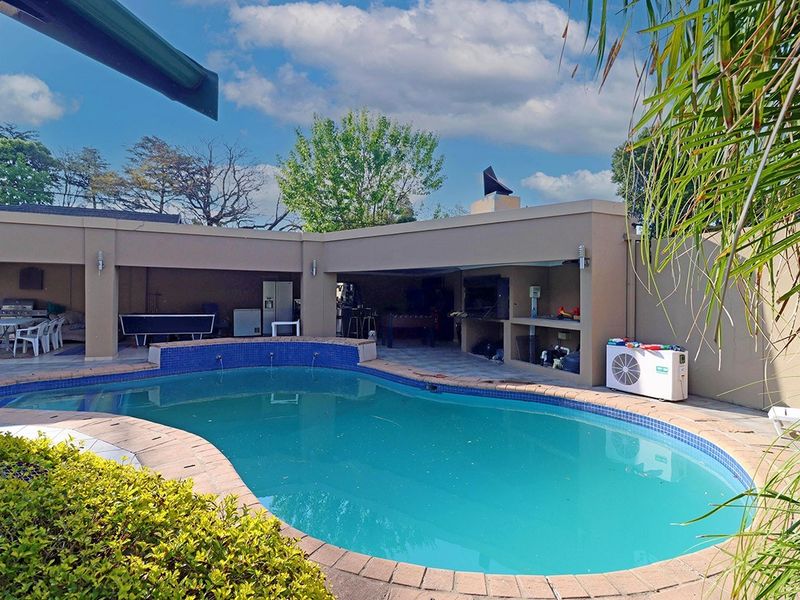 Outdoor entertainment area featuring a swimming pool with water features and a covered patio with a built-in braai.