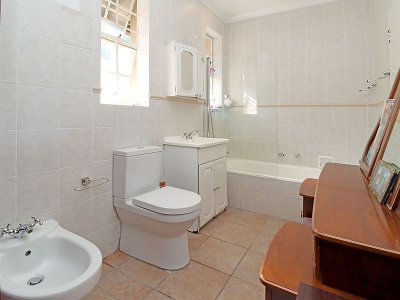 A functional bathroom featuring a bathtub with a glass screen, a vanity basin, a toilet, and a bidet, finished with neutral wall and floor tiles.