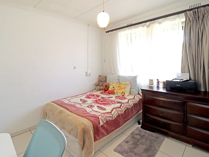 A functional bedroom featuring tiled flooring, a large window with curtain rails, and a central pendant light fixture.