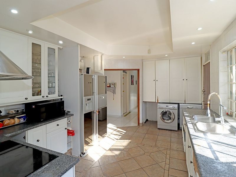 Spacious kitchen featuring white cabinetry, granite countertops, integrated laundry appliances, and tiled flooring with ample natural light.