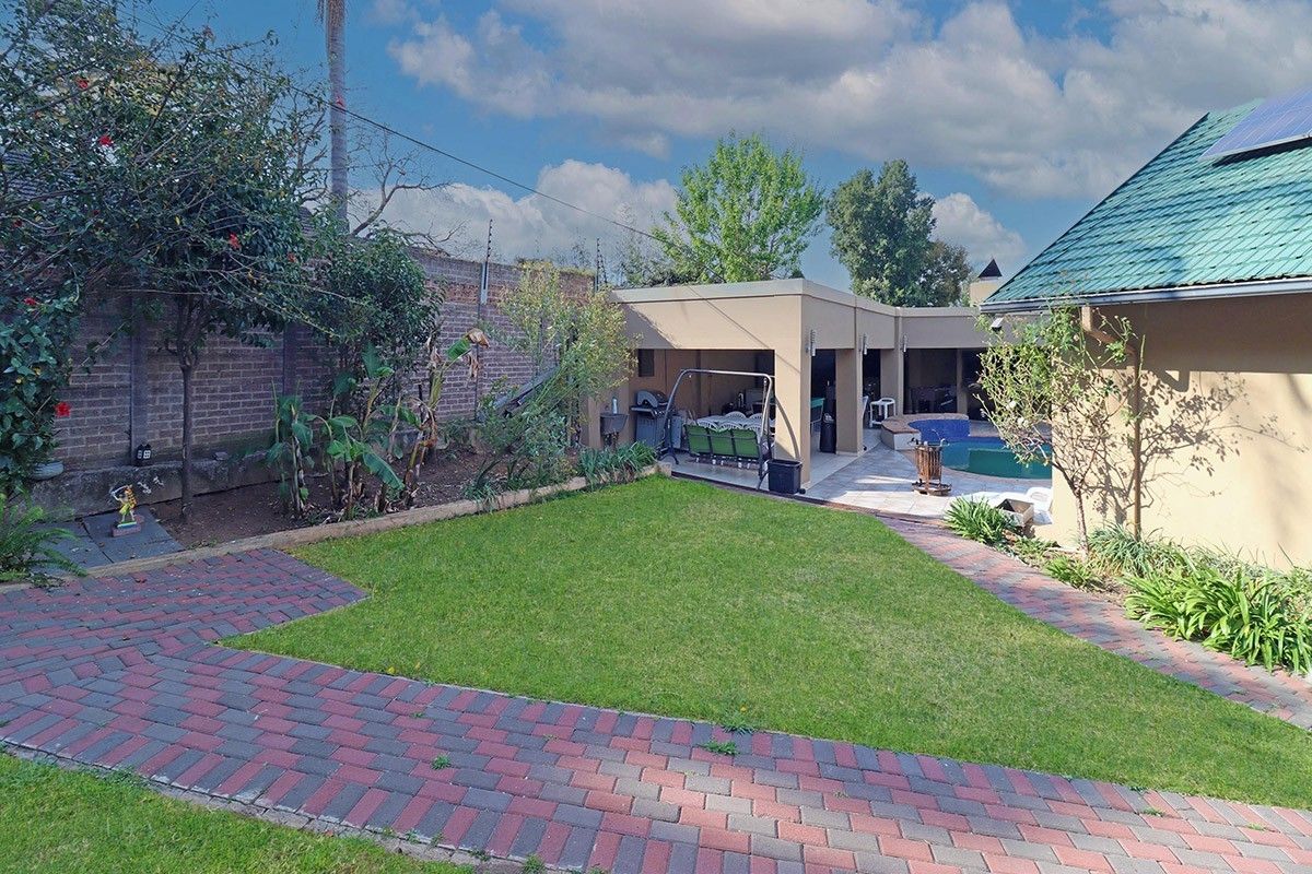 A well-maintained rear garden featuring a lawn, brick pathways, a covered patio area, and a swimming pool, enclosed by a secure boundary wall.