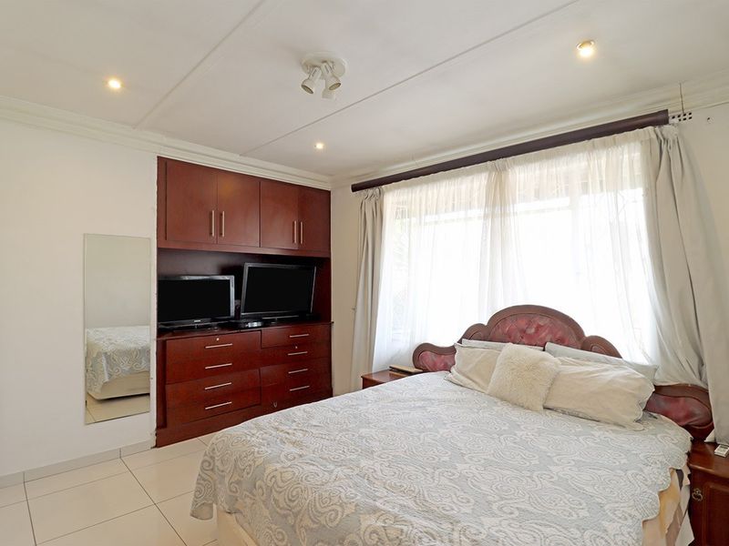 A bedroom featuring built-in wooden cabinetry, tiled flooring, and recessed ceiling lighting, offering a functional and well-maintained living space.