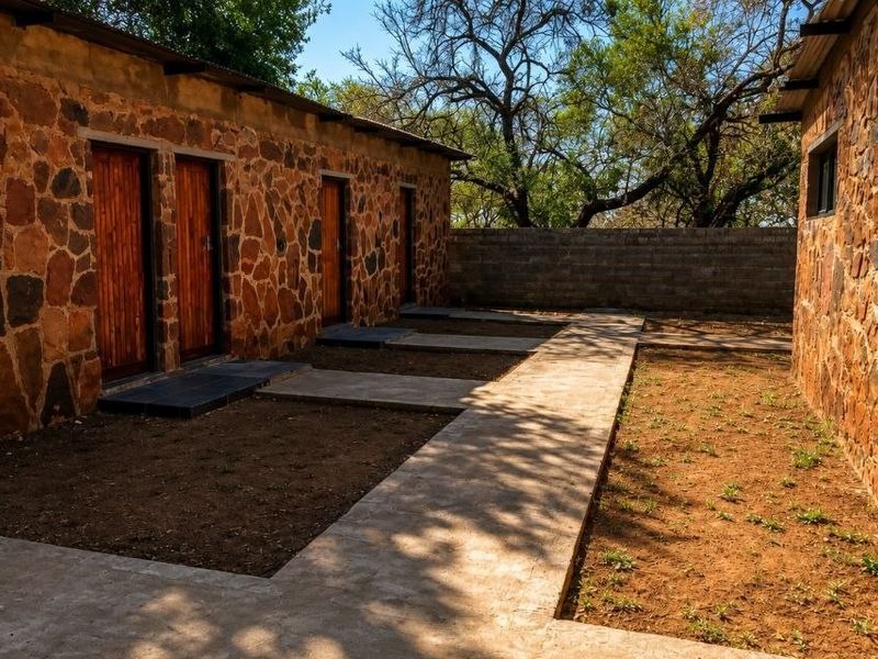 A rear exterior view of a farm-style building featuring rustic stone cladding, timber doors, and a concrete pathway leading between structures.