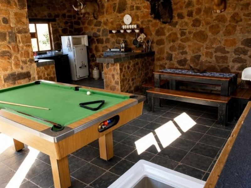 Covered outdoor entertainment area featuring rustic stone walls, tiled flooring, a built-in stone bar counter, and corrugated metal roofing.