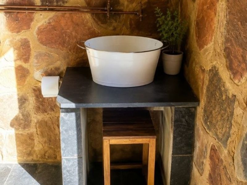 A rustic bathroom featuring natural stone wall cladding, slate flooring, a stone vanity with a basin, and exposed copper plumbing fixtures.