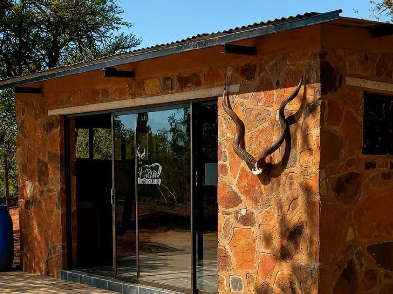A rustic farm-style building featuring natural stone cladding, a corrugated metal roof, and modern sliding glass doors opening onto a concrete patio.
