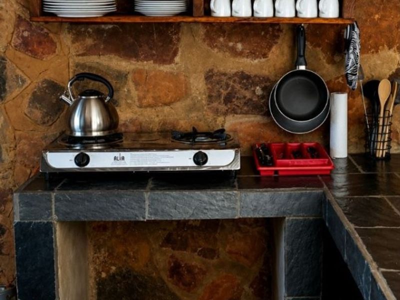 Rustic kitchen area featuring natural stone walls, slate tile countertops, and a built-in stone base with a gas cooktop.