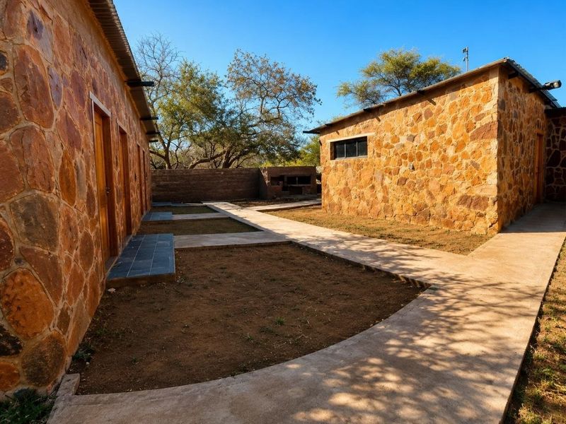 Rear courtyard area featuring stone-clad buildings, concrete walkways, and a built-in outdoor braai facility within a rural farm setting.