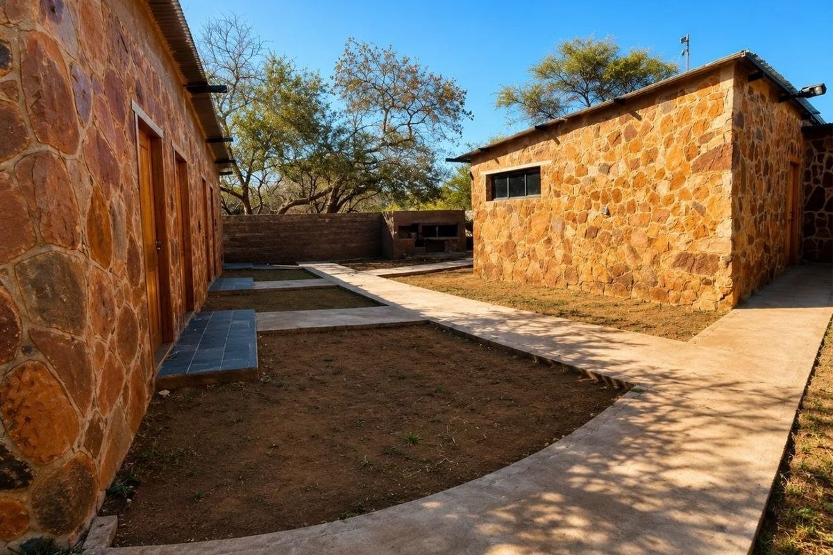 Rear courtyard area featuring stone-clad buildings, concrete walkways, and a built-in outdoor braai facility within a rural farm setting.