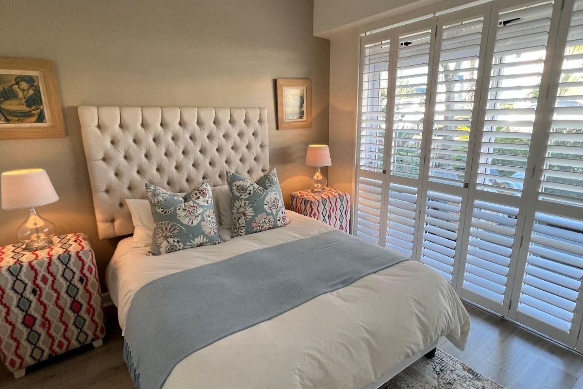 A well-maintained bedroom featuring light laminate flooring, recessed ceiling lighting, and white plantation shutters providing natural light control.