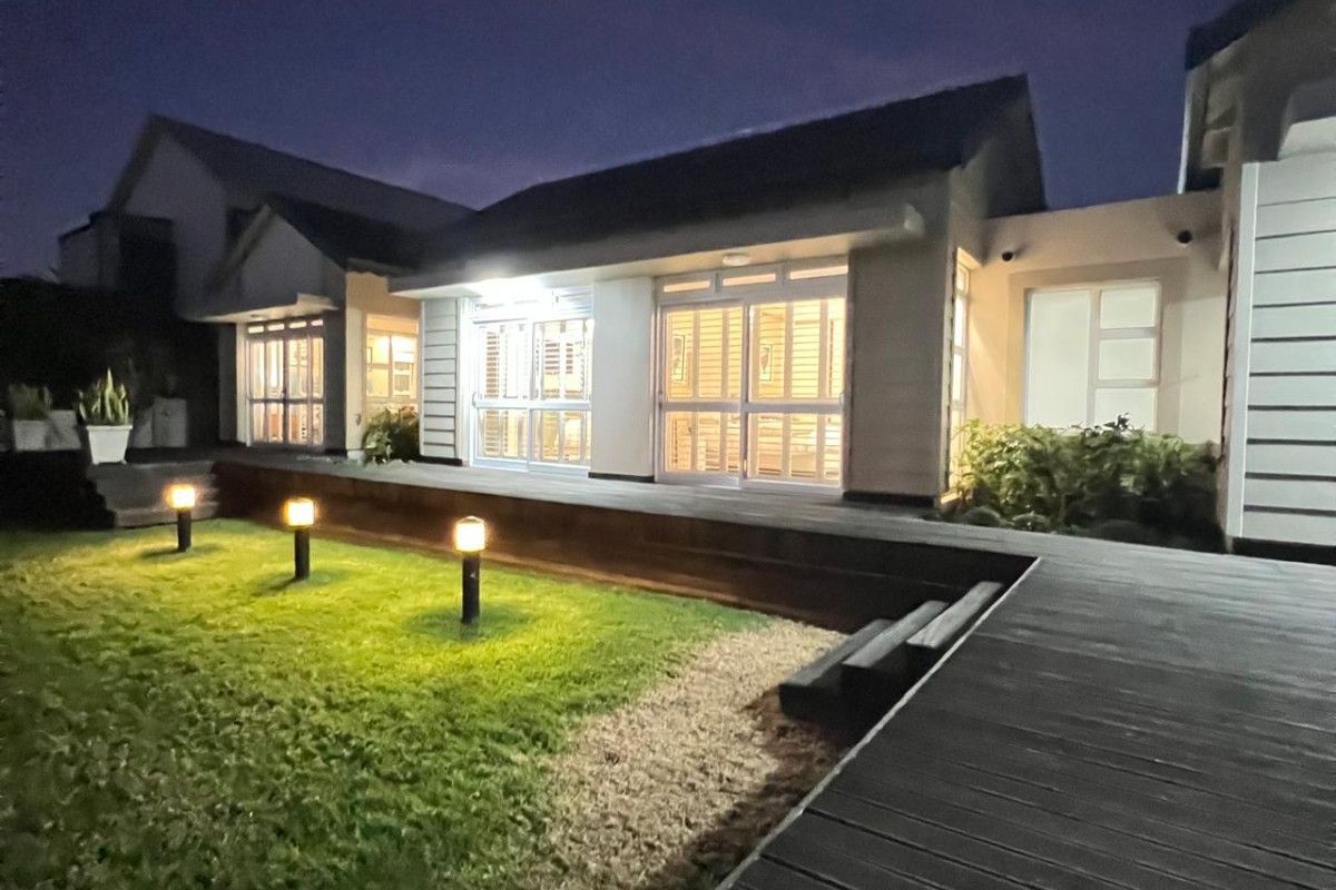A well-maintained rear exterior view featuring timber decking, a landscaped lawn with garden lighting, and large sliding glass doors leading into the home.