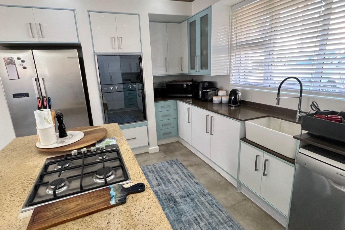 Modern kitchen featuring a central island with gas cooktop, farmhouse sink, stone countertops, and ample built-in cabinetry with a clean, contemporary finish.