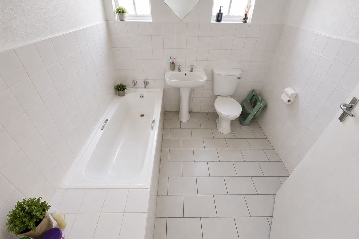 A clean, functional bathroom featuring a built-in bathtub, pedestal basin, and toilet, finished with neutral white wall tiles and light grey floor tiles.