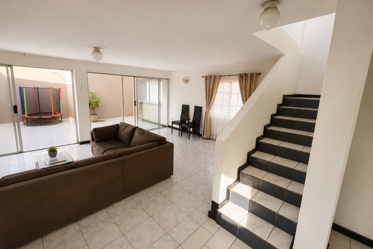 Spacious open-plan living area featuring tiled flooring, a central staircase, and large sliding glass doors providing access to an outdoor patio space.