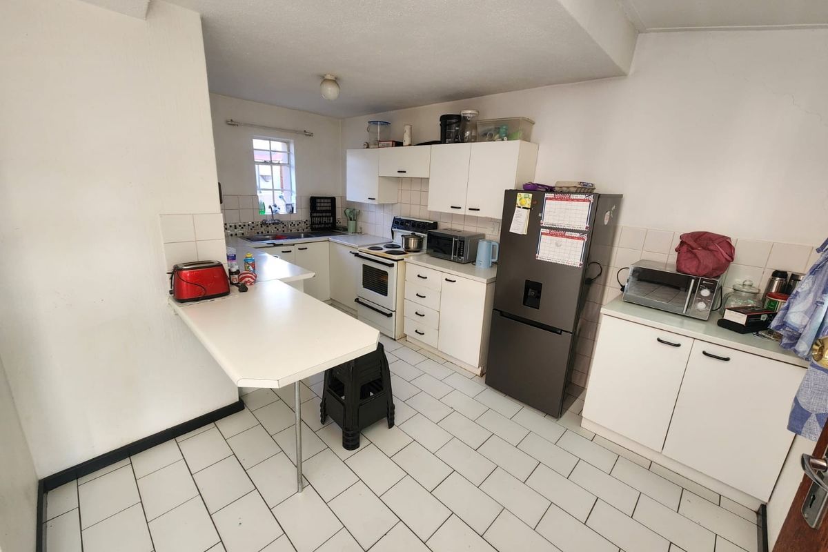 A functional kitchen featuring white cabinetry, tiled flooring, a breakfast counter, and built-in cooking appliances, offering potential for modernization.